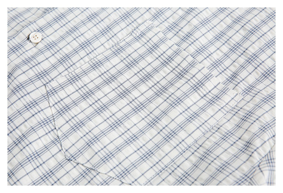 Close-up of a white shirt with a blue-gray plaid pattern, showing a button and chest pocket.