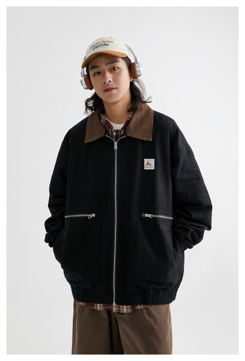 Front view of a model wearing a black zip jacket with a brown collar, two zip pockets and a chest patch.