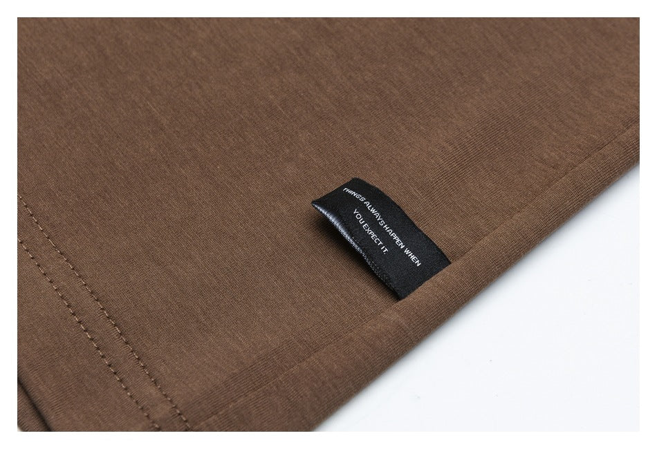 Close-up of a brown garment hem with double stitching and a small black woven tag bearing white English text.