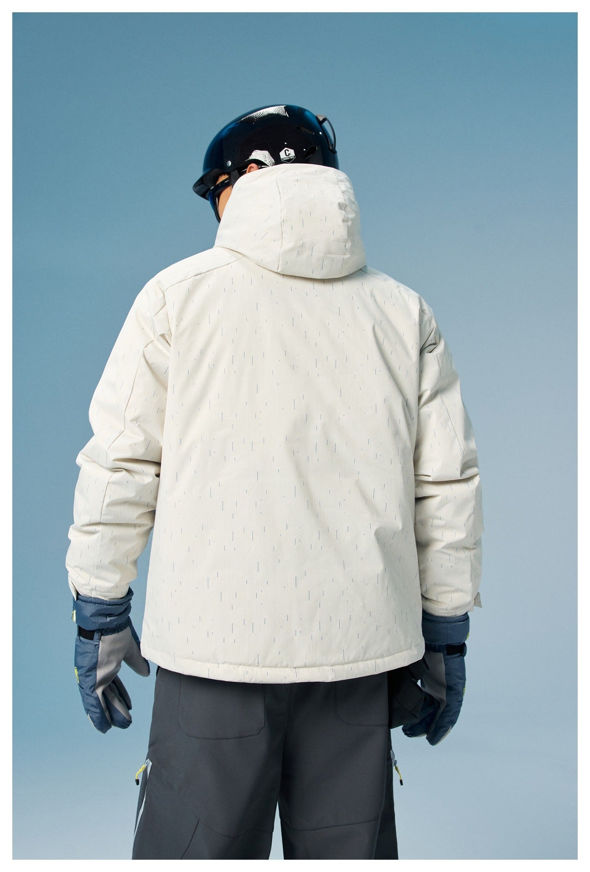 Back view of a model wearing a white patterned hooded ski jacket, dark snow pants and blue gloves.