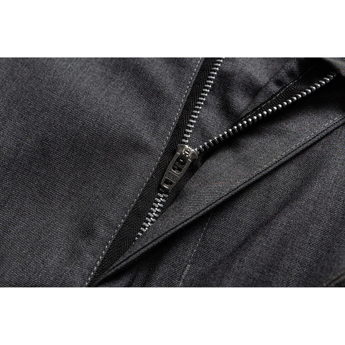 Macro view of a metal zipper and stitched fly on dark gray woven trousers.
