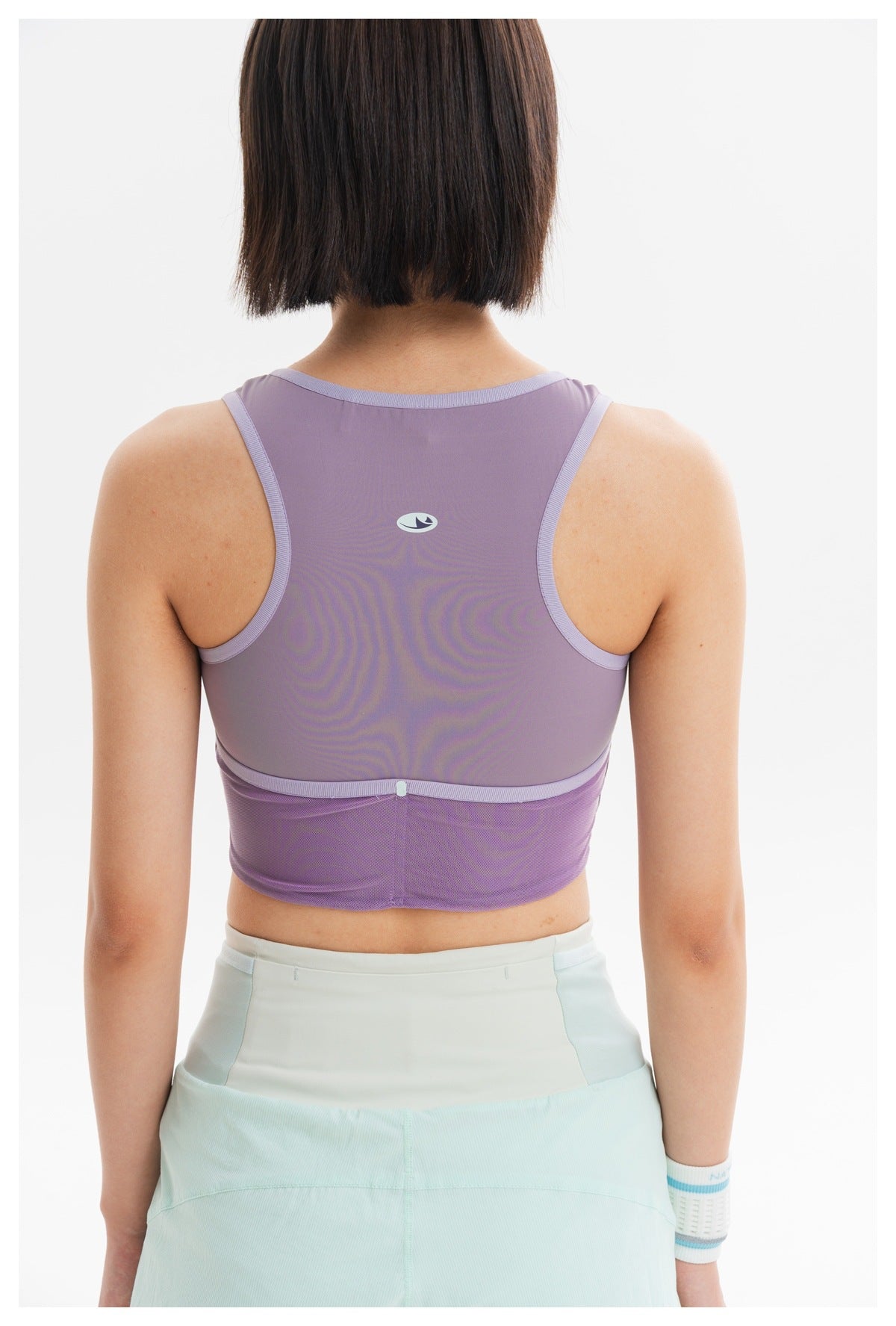 Back view of a model wearing a lavender cropped athletic tank with mesh panels and pale mint shorts.