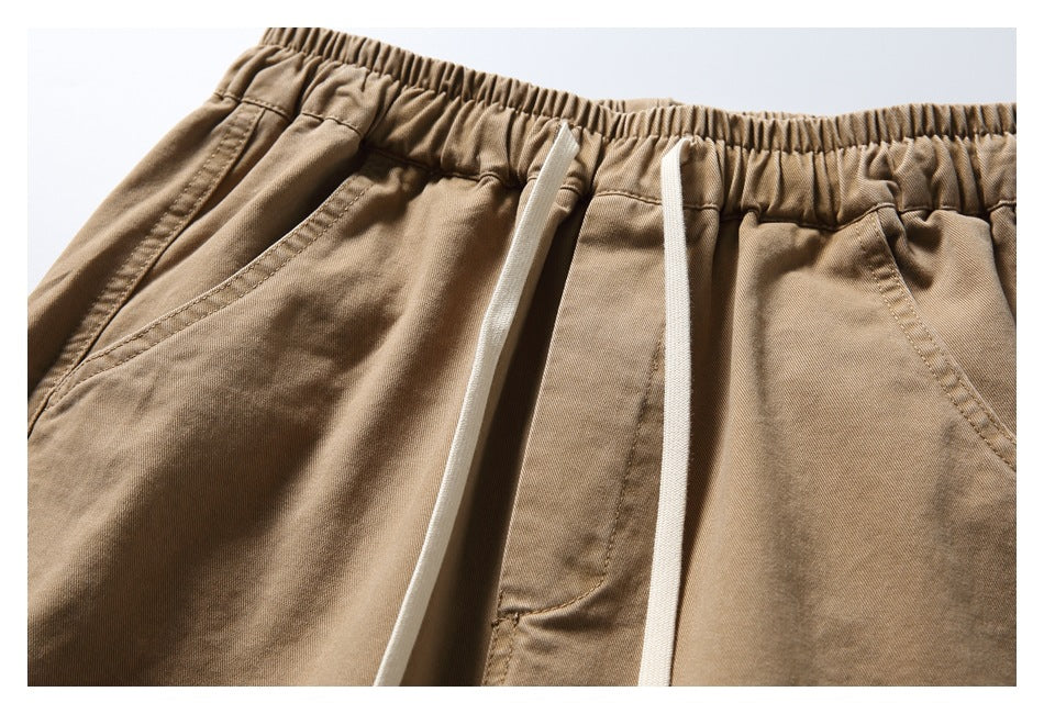 Close-up of tan trousers showing the elastic waistband, white drawstrings, and angled front pockets.