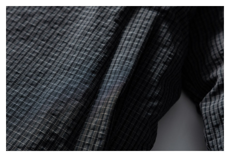 Close-up of dark charcoal plaid garment fabric with fine gray and white intersecting lines.