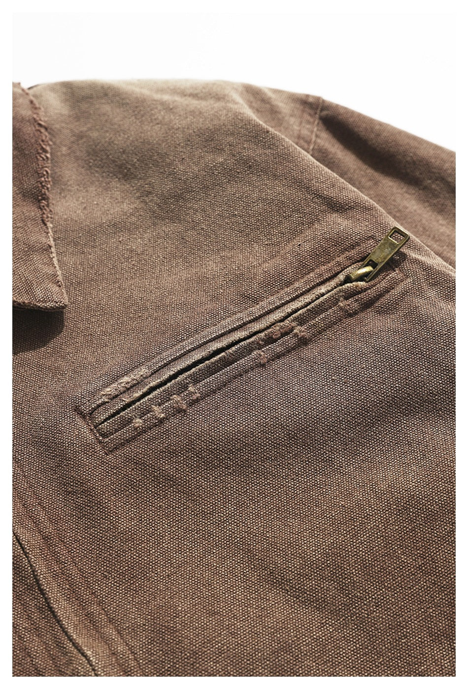 Close-up of a brown textured garment with a diagonal brass-tone zip pocket and stitched collar edge.