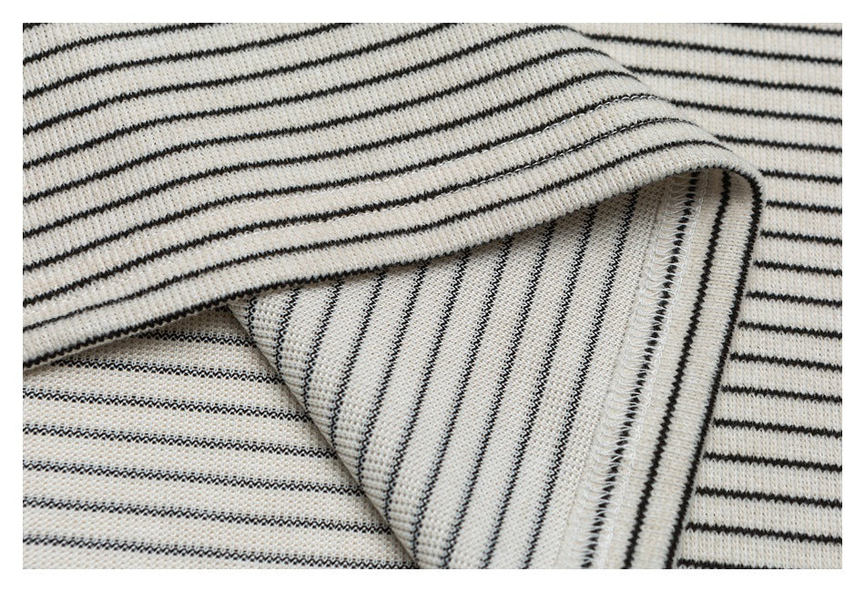Close-up of cream knit fabric with thin black stripes, folded to show an overlocked seam.