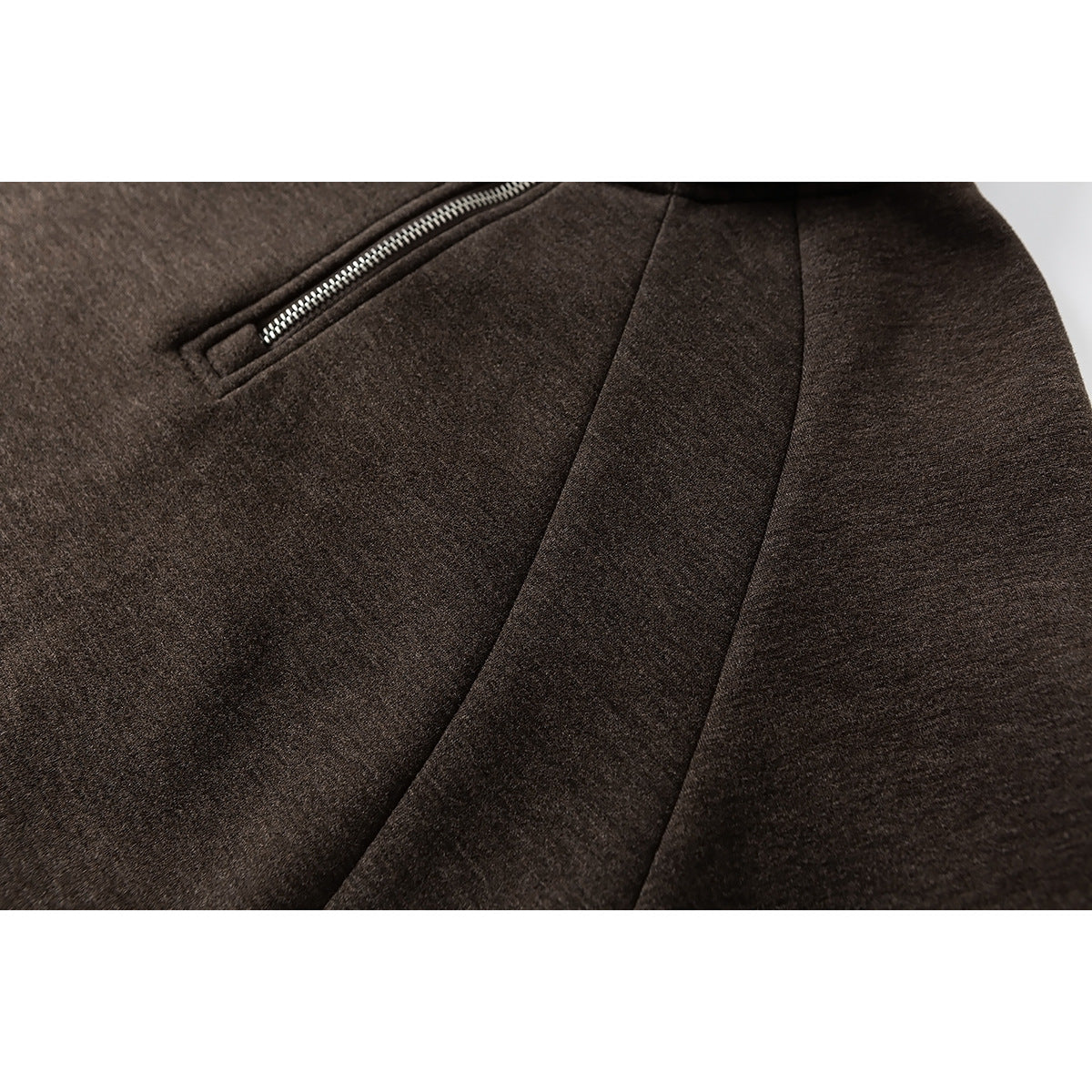 Close-up of dark brown fabric, a silver zip pocket, and curved panel seams.