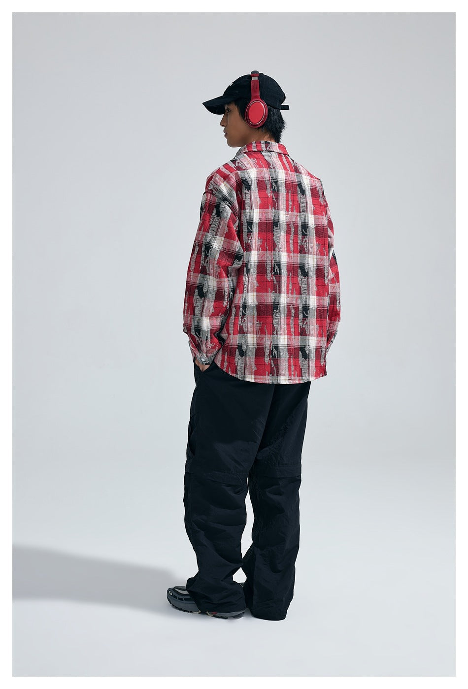 Rear view of a model wearing a red, black, and white plaid button-up shirt and black pants.