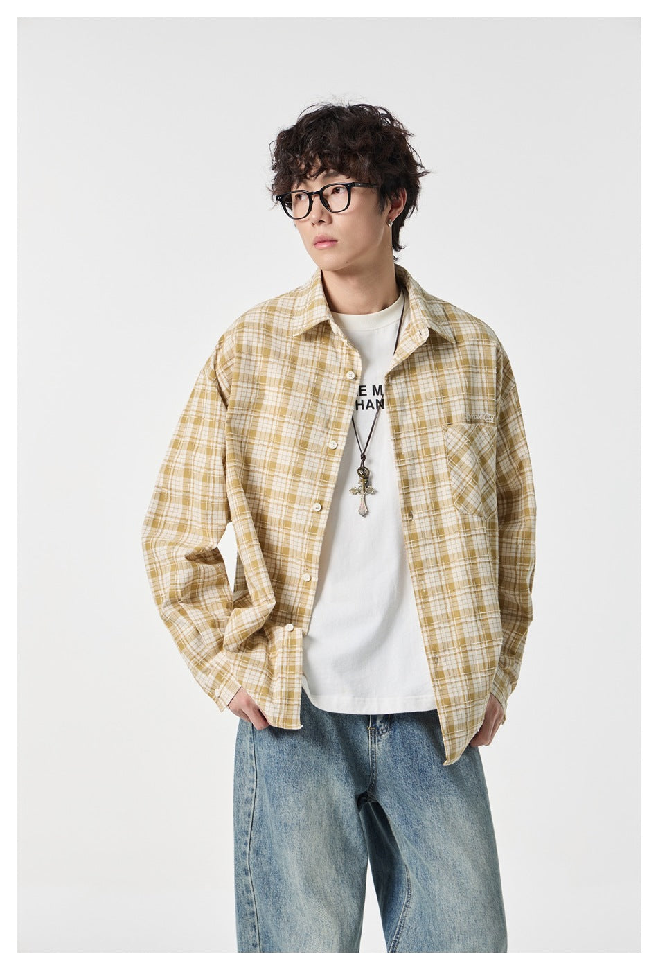 Model wearing an open mustard and cream plaid button-up shirt over a white tee with loose blue jeans.