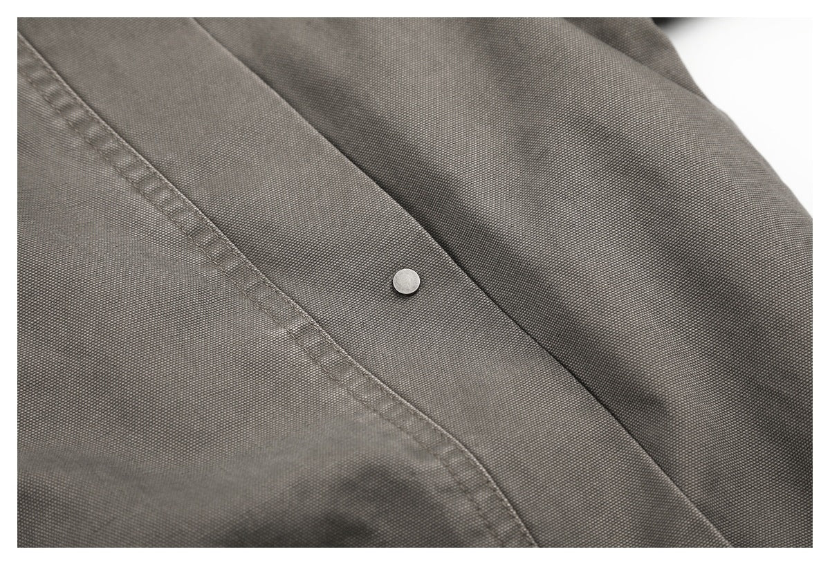 Close-up of a round metal snap on a charcoal-gray garment beside a stitched seam.