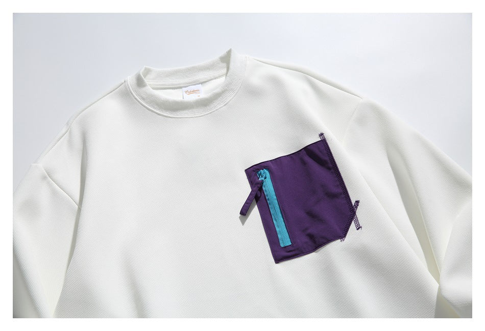 White crewneck sweatshirt laid flat, with long sleeves and a purple chest pocket featuring a turquoise zipper.