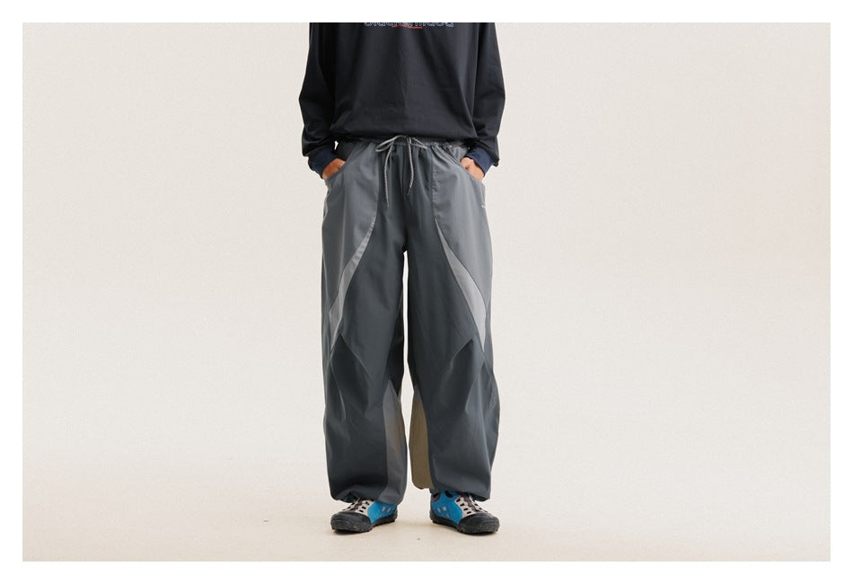 Front view of a model wearing loose charcoal-gray paneled pants with a drawstring waist and side pockets.