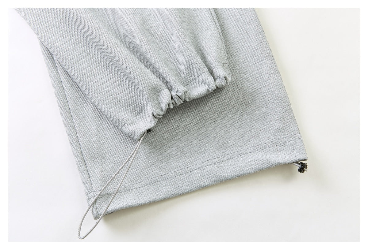 Close-up of a pale gray garment hem with gathered fabric and a long cord drawstring.