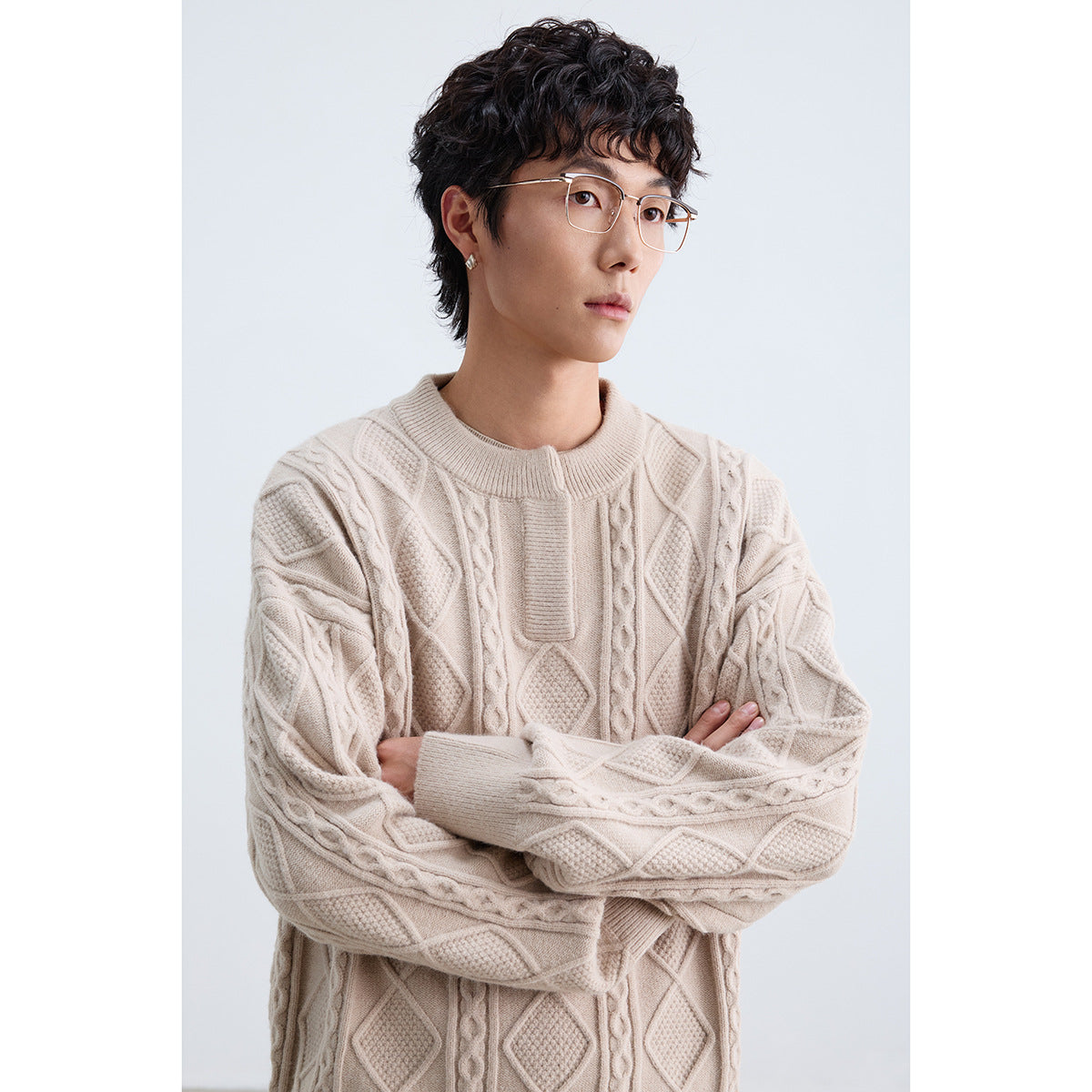 Model wearing a cream cable-knit sweater with raised diamond and cable patterns, a ribbed crew neck, and a short front