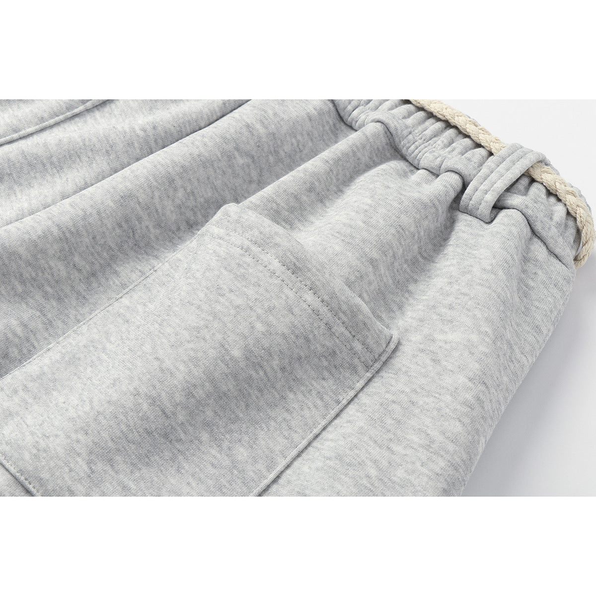Close-up of a front pocket and elastic waistband on light gray heathered sweatpants, with a cream drawstring.