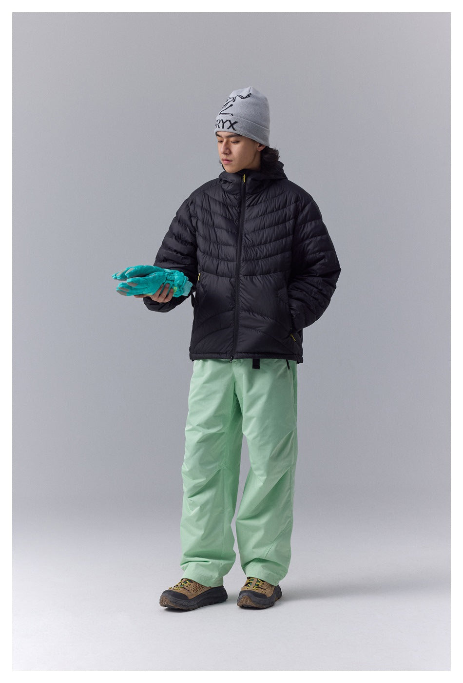 Front view of a model wearing a black hooded quilted jacket and mint-green snow pants.