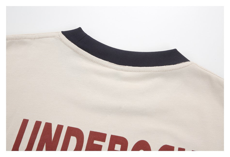 Close-up of a beige shirt's dark ribbed crew neckline and partial red lettering.