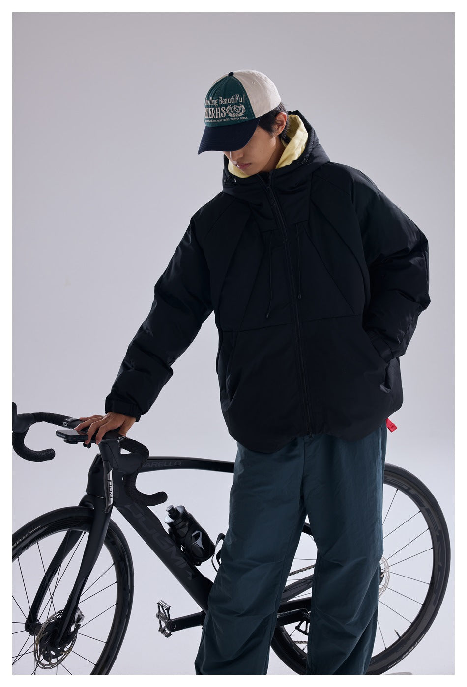 Angled view of a model wearing a black hooded puffer jacket beside a bicycle.