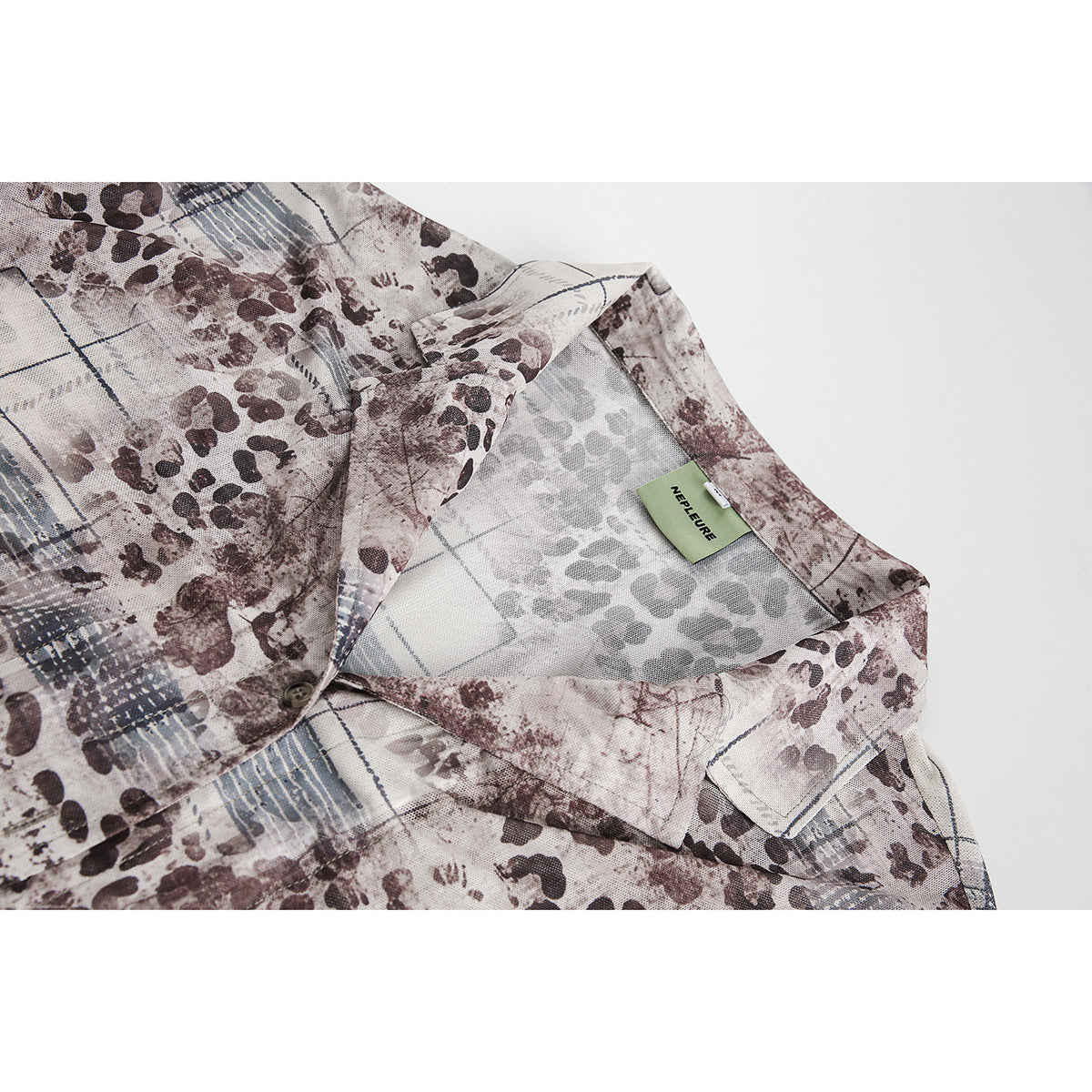 Close-up of a collared shirt with an abstract brown, gray, and blue print and a small green neck label.