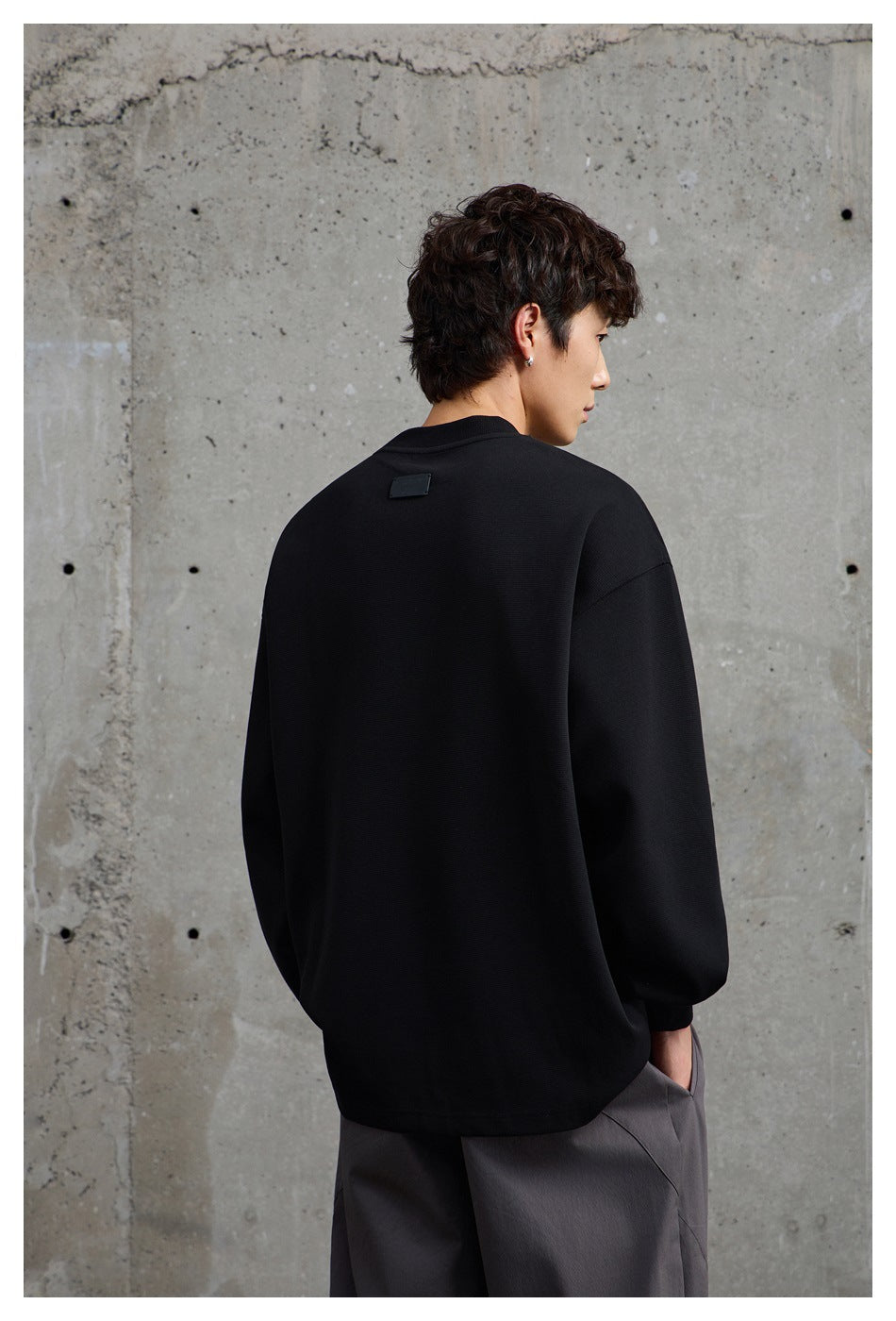 Model shown from behind in a black oversized crewneck sweatshirt with a small blank patch near the collar.