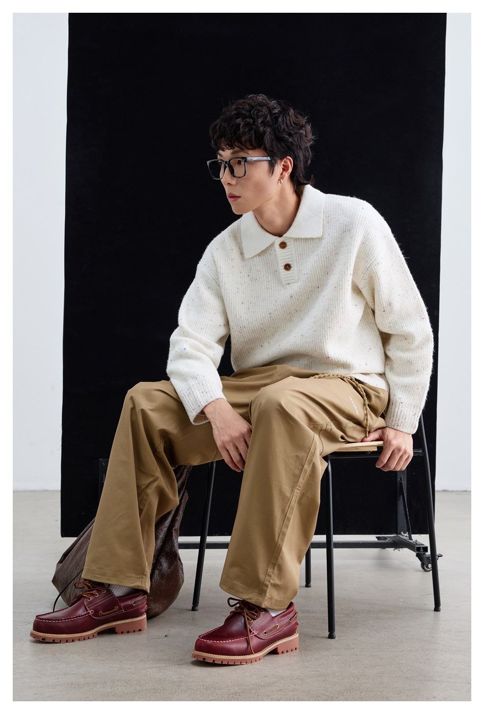 Model seated in an ivory flecked knit polo sweater, tan trousers, and burgundy lace-up shoes.