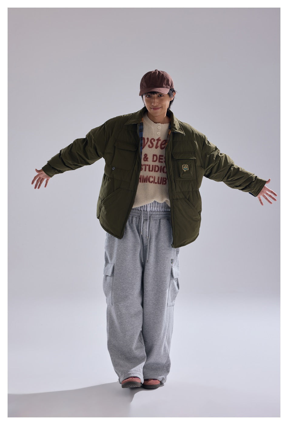 Model facing forward in an olive quilted jacket with flap pockets and loose gray cargo pants.