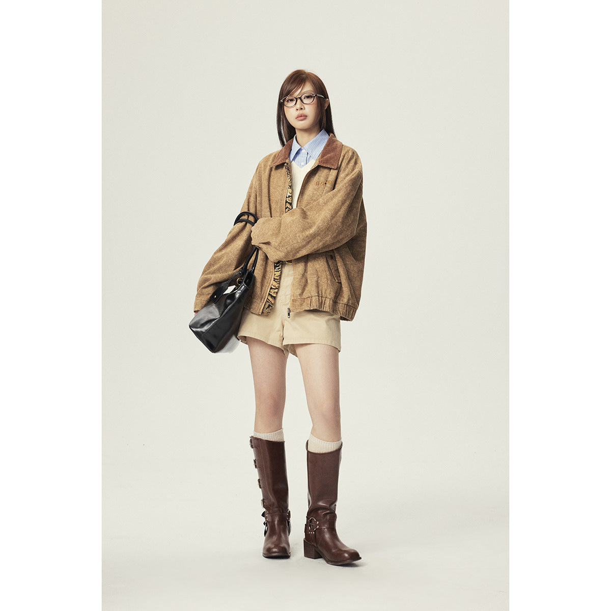 Front view of a model in an oversized tan jacket, beige shorts, and tall brown boots.