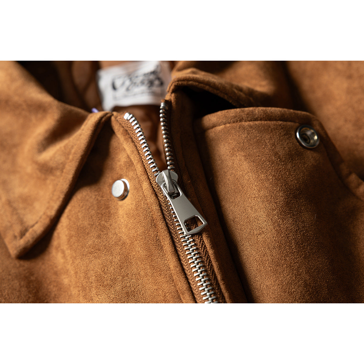 Close-up of a brown jacket showing its silver front zipper, snap fasteners, and textured surface.