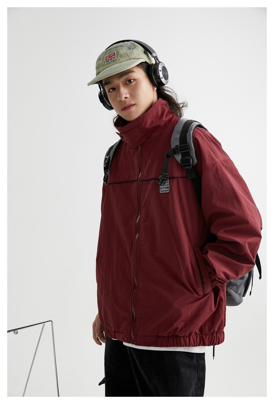 Model wearing a burgundy zip-front jacket with a high collar, black chest piping, elastic hem and cuffs, and side pockets.