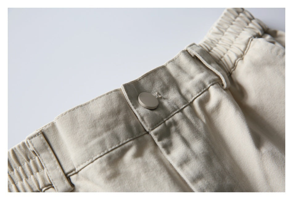 Close-up of light beige pants showing the button closure, belt loop, and gathered elastic waistband.