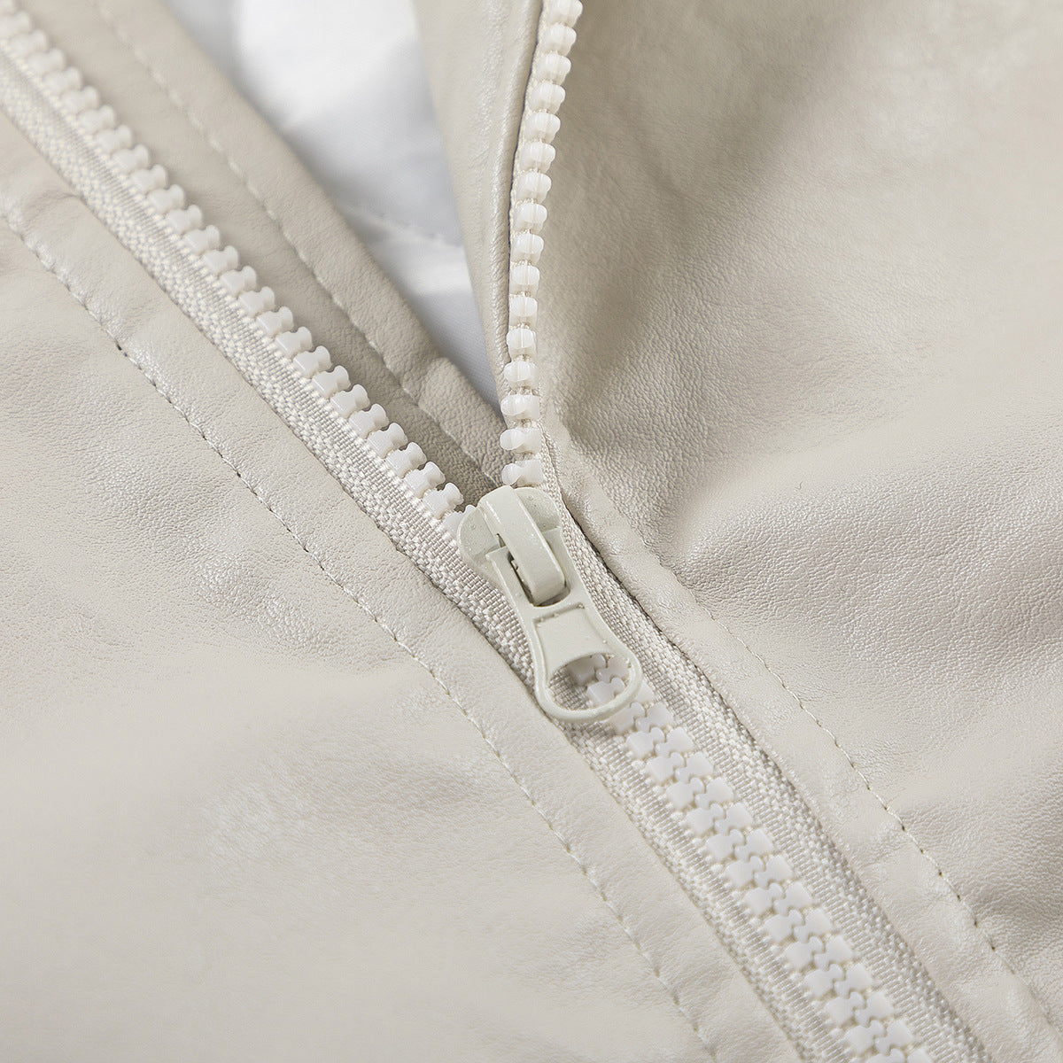 Close-up of the ivory jacket's chunky front zipper and surrounding stitched panels.