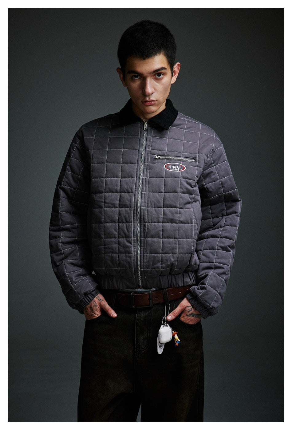 Mid-length front view of a model wearing a charcoal-gray quilted jacket with a black collar and zip chest pocket.