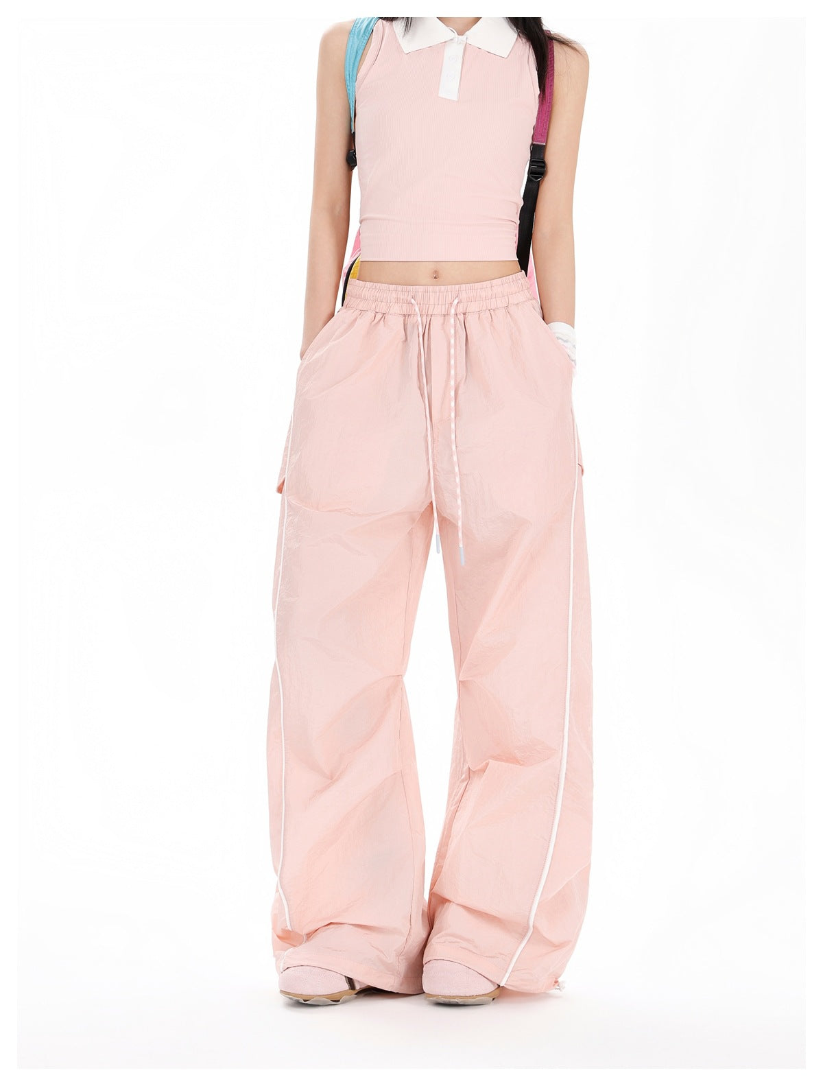 Front view of a model wearing pale pink wide-leg drawstring pants with white piping and side flap pockets.
