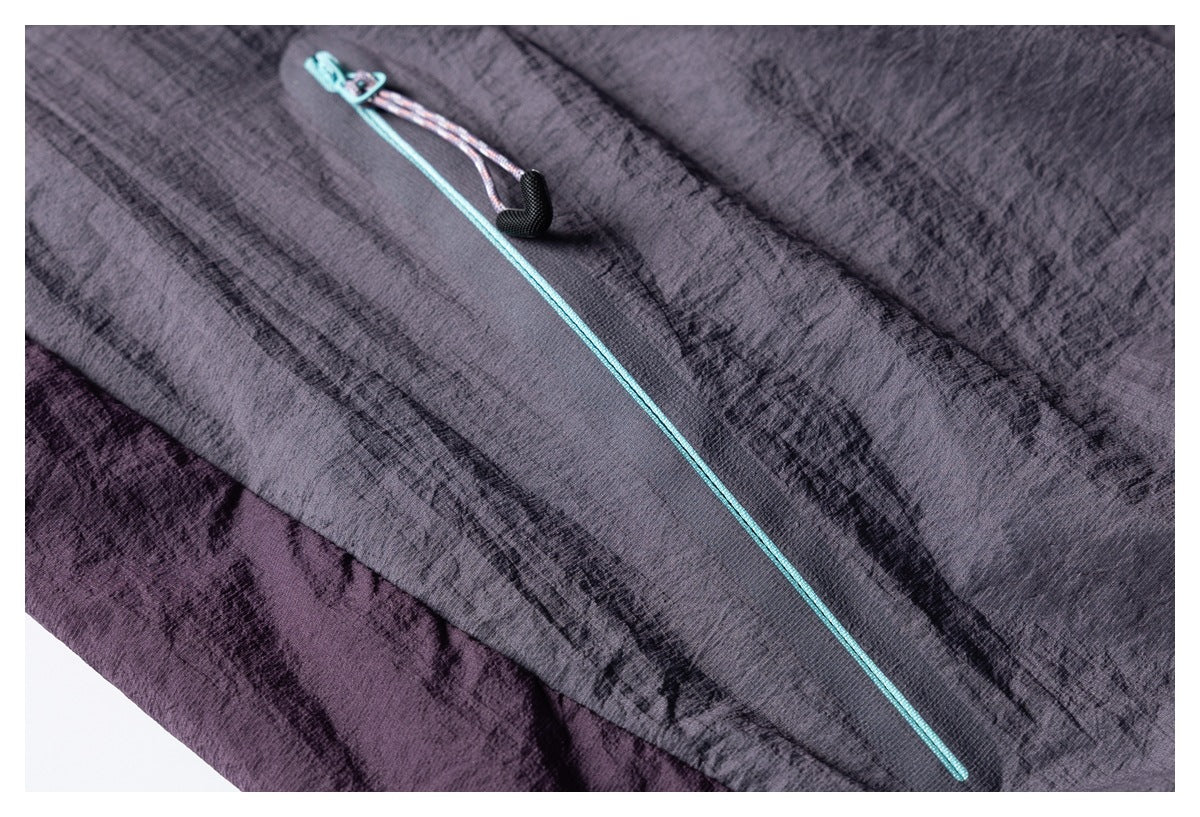 Close-up of a jacket panel with a long turquoise zipper and black pull against dark gray-purple fabric.