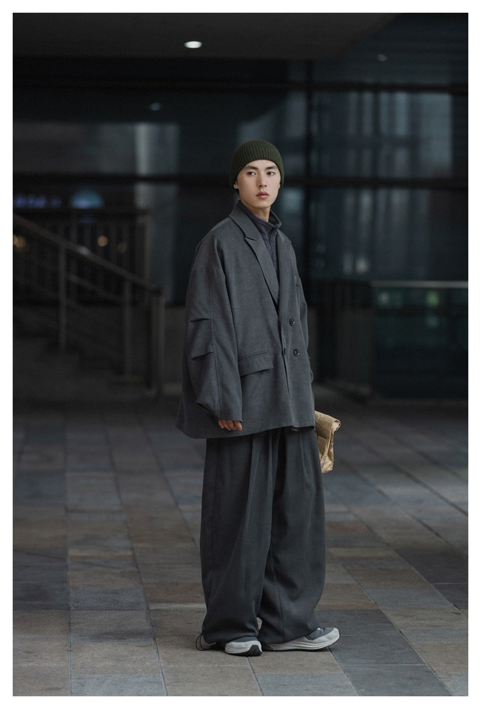 Man modeling an oversized charcoal-gray double-breasted blazer with wide-leg trousers and an olive ribbed beanie.