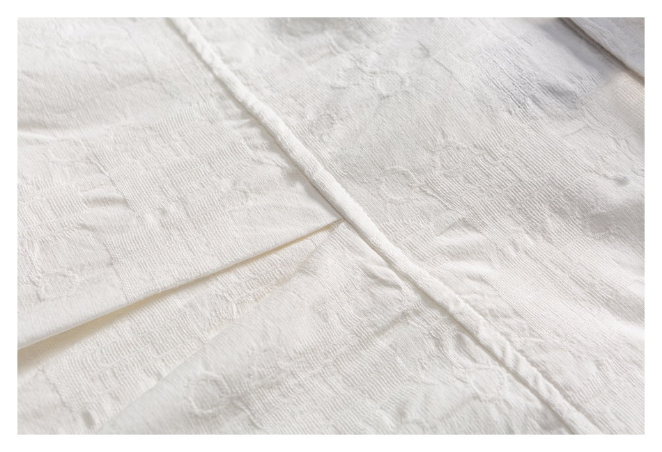 Close-up of ivory-white fabric laid in overlapping folds, showing a subtle woven texture.