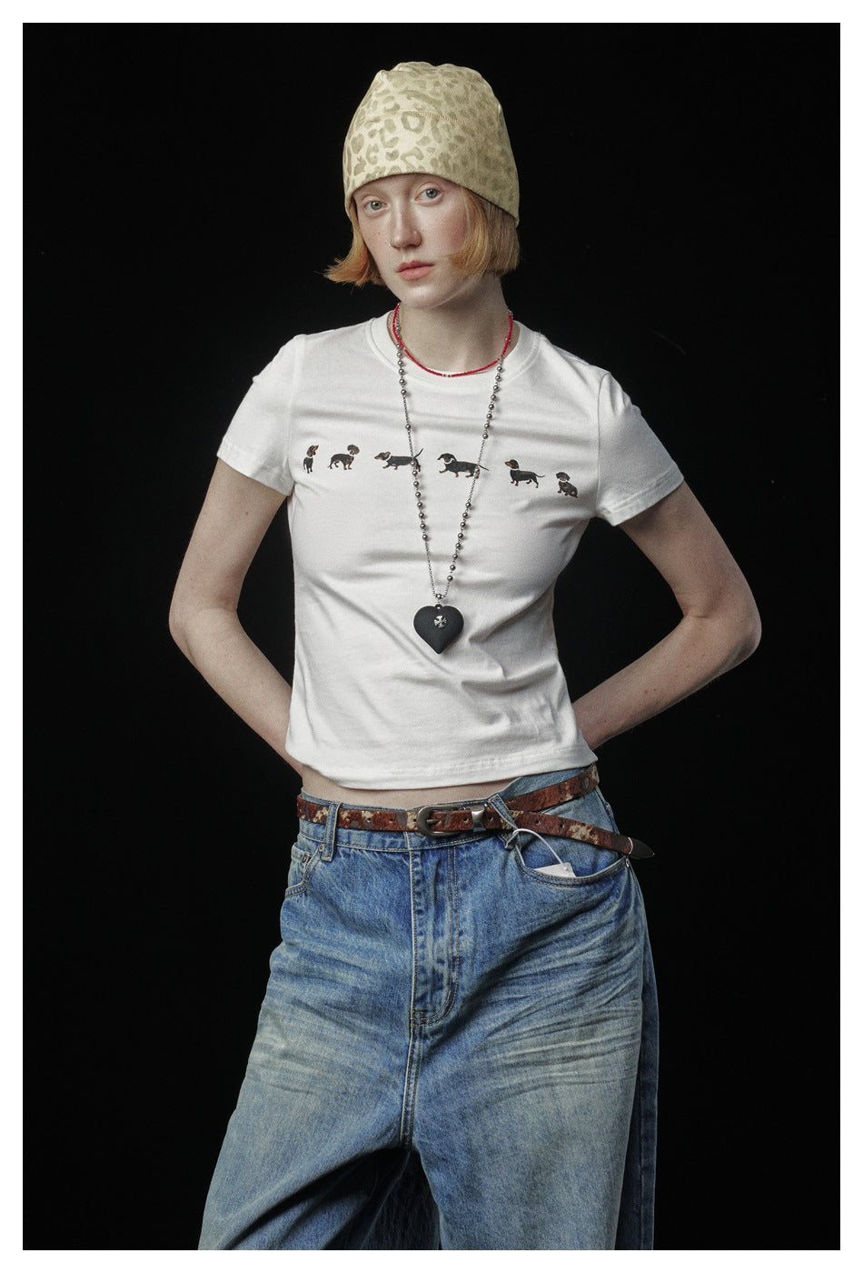 Model wearing a white dachshund-print T-shirt with loose blue jeans and a beige patterned beanie.