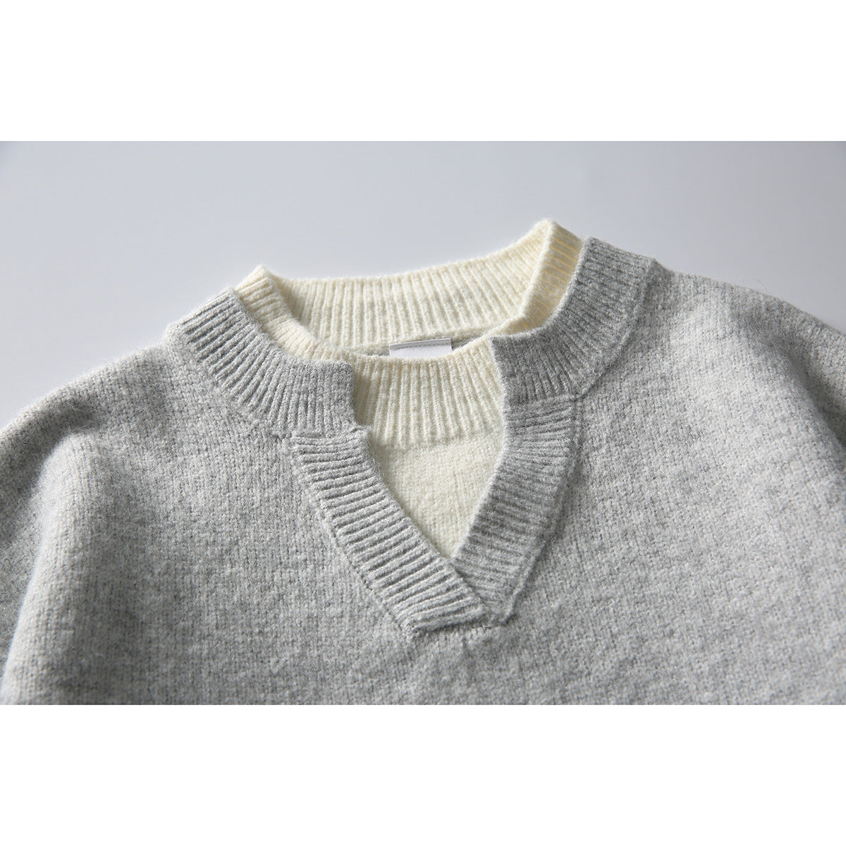 Close-up of a gray V-neck knit sweater layered over a cream ribbed crew-neck sweater.