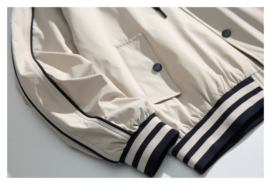 Close-up of an ivory jacket with a snap-flap pocket, dark piping, and striped dark-and-ivory ribbed cuffs and hem.
