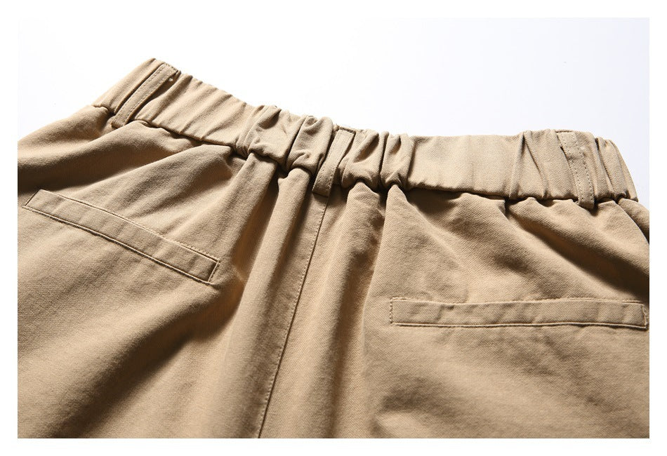 Close-up of tan trousers with a gathered elastic waistband and two rear welt pockets.