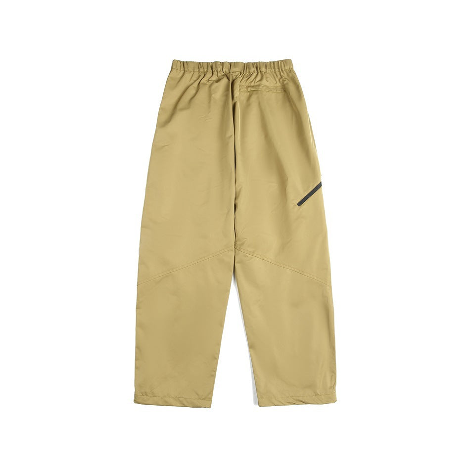 Back view of tan loose-fit pants with an elastic waist, small rear pocket, and diagonal black leg detail.
