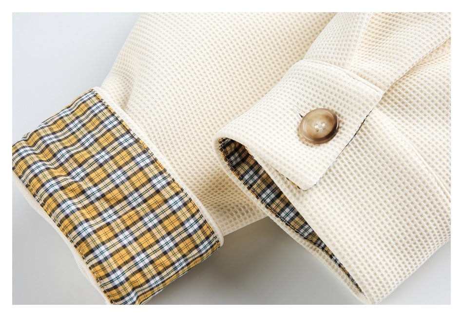 Close-up of an ivory textured shirt cuff with a brown button and yellow, black, and white plaid lining.