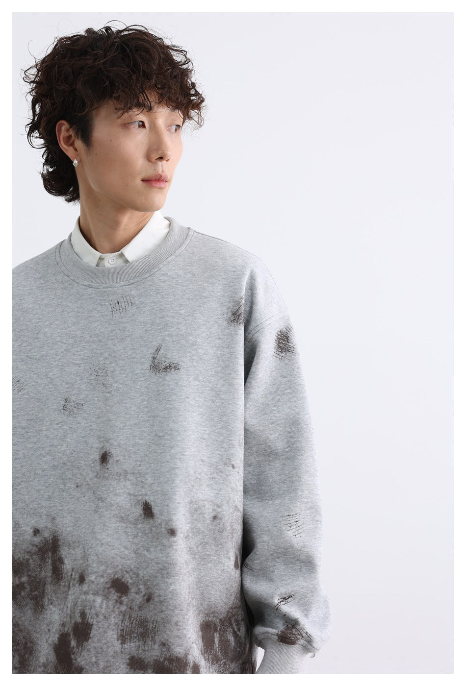 Close view of a light gray sweatshirt with scattered dark distressed marks, worn over a white collared shirt.