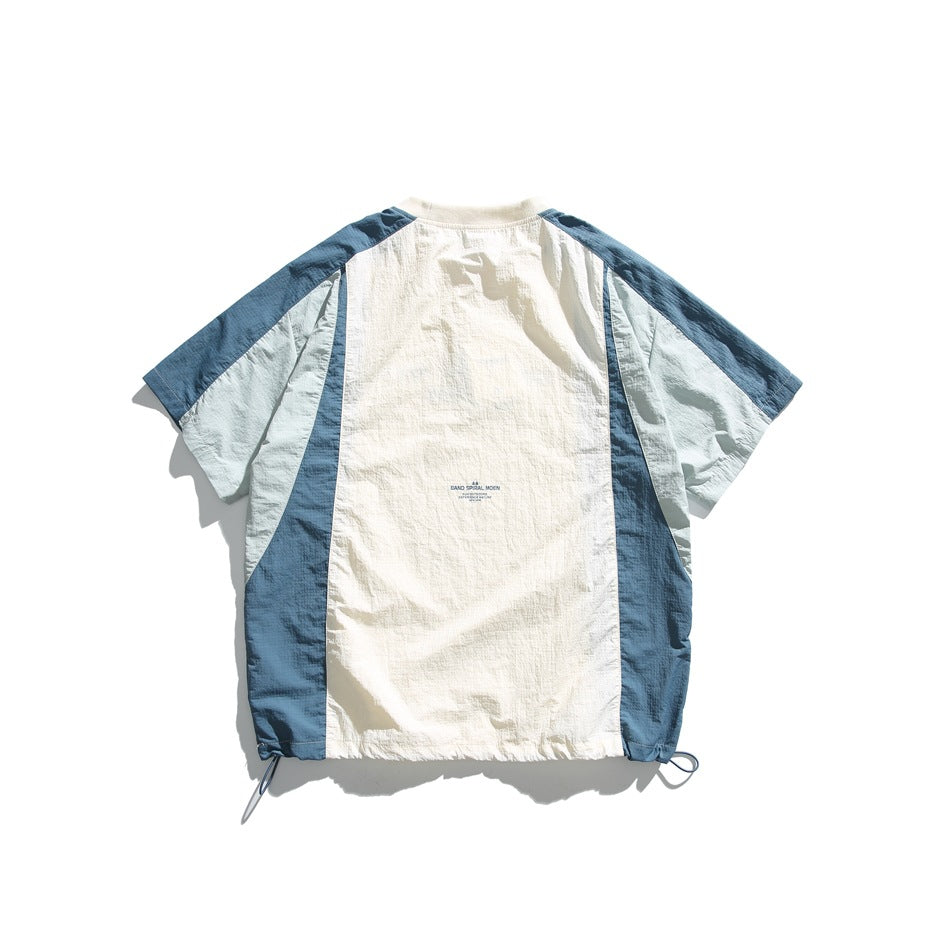 Flat-lay back of a cream color-block shirt with blue and pale sage panels, short sleeves, and adjustable hem cords.