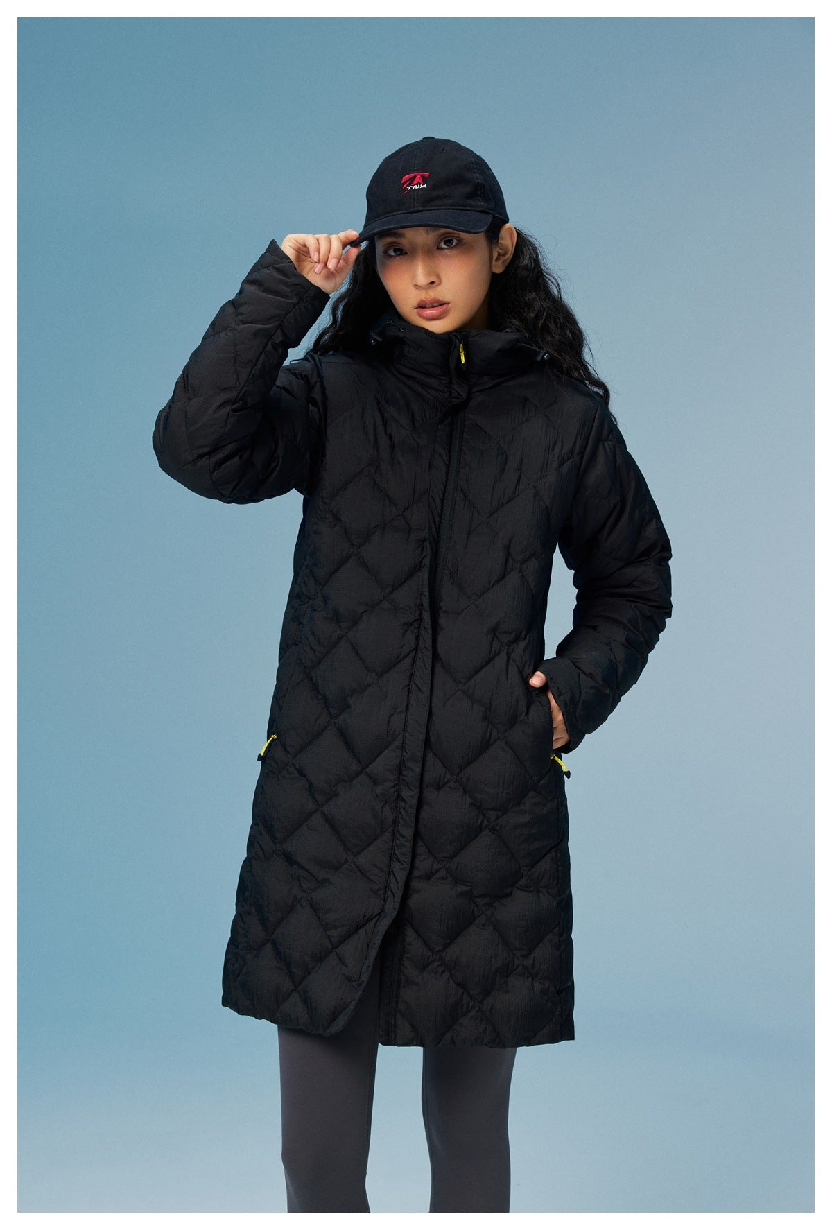 Front view of a woman wearing a black knee-length diamond-quilted coat with yellow zipper pulls.