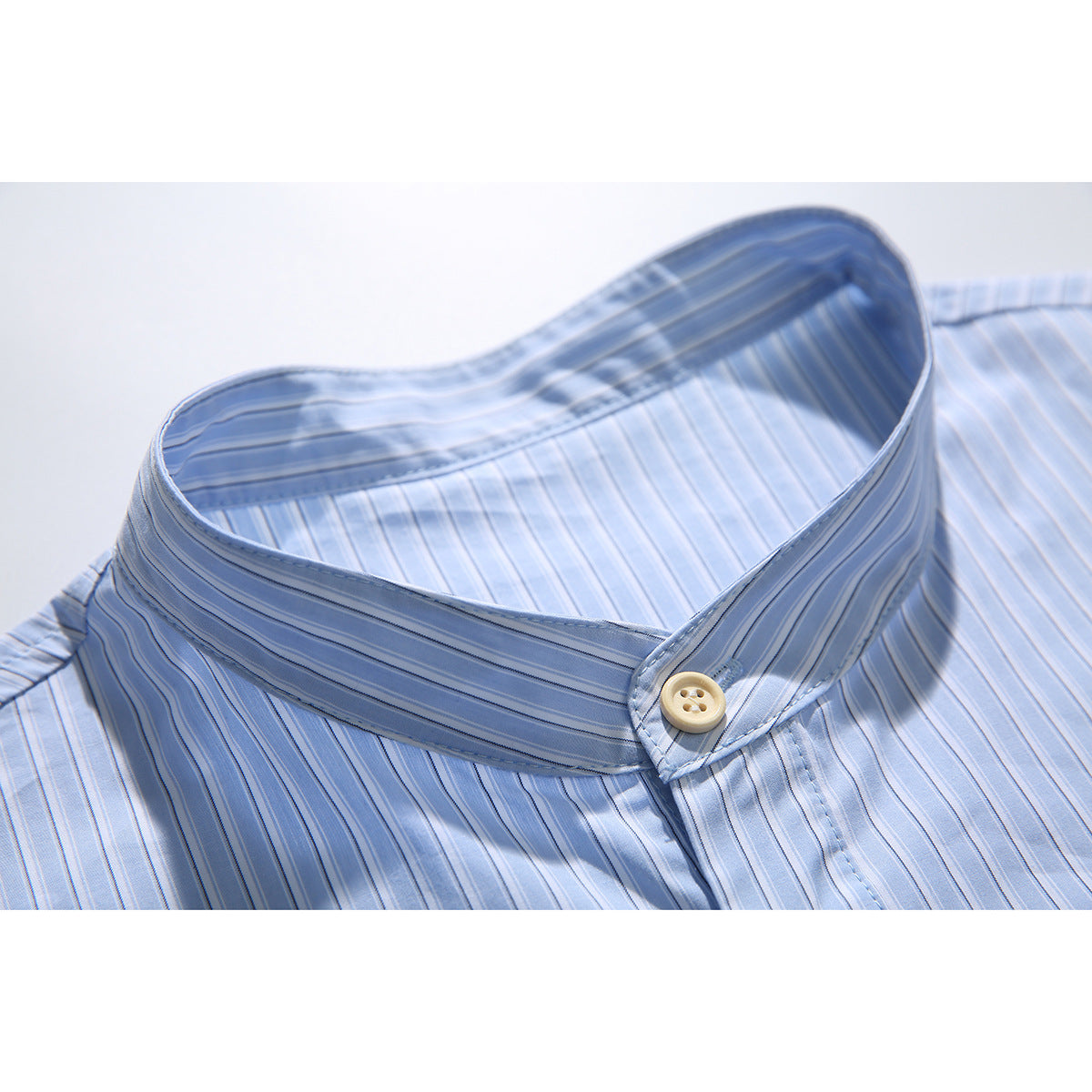 Close-up of a light blue striped shirt's stand collar and cream button.