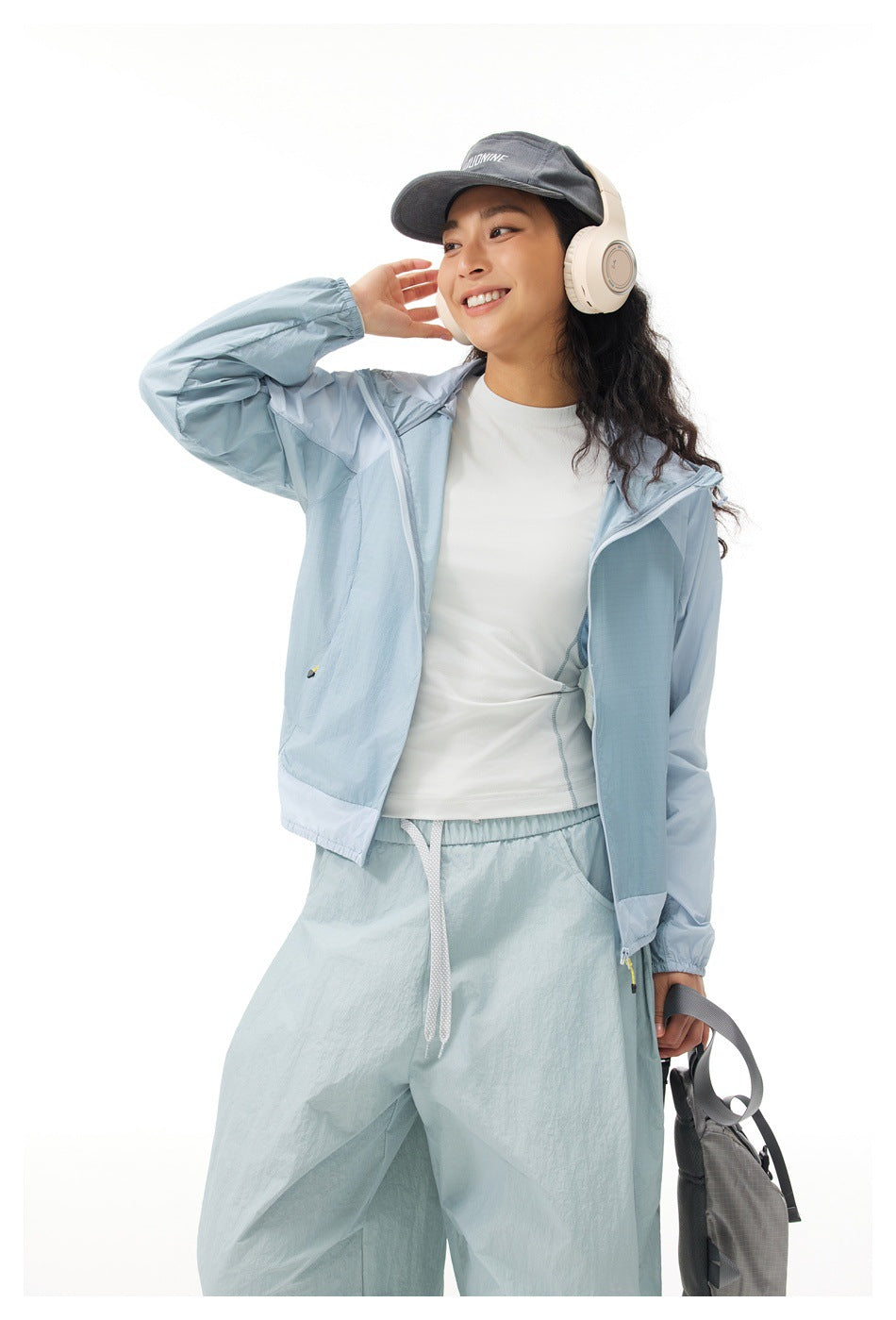 Model wearing an open light blue hooded jacket and loose pale blue pants, with a white top.