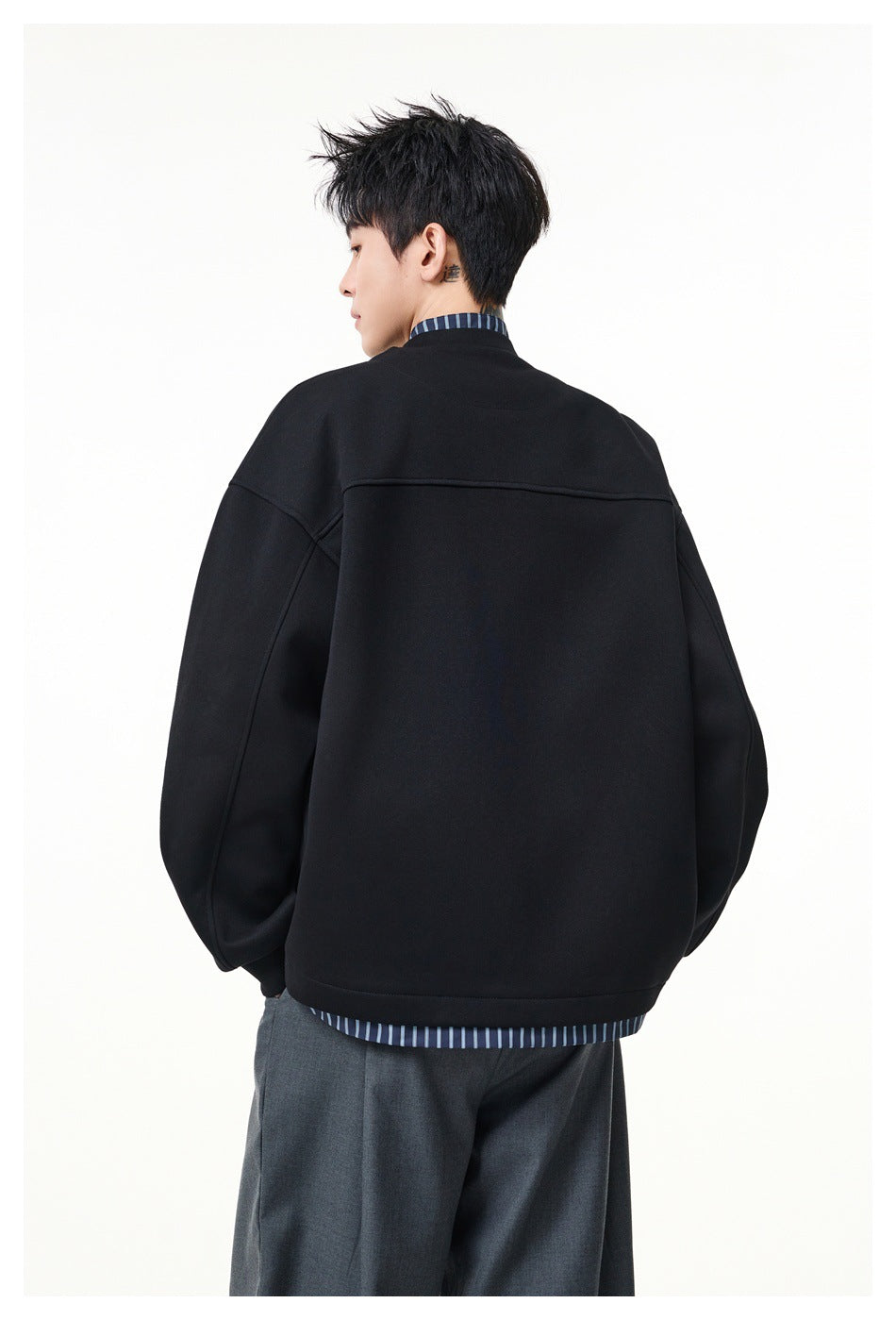 Back view of a model wearing a black oversized jacket, with a blue striped shirt visible at the collar and hem.