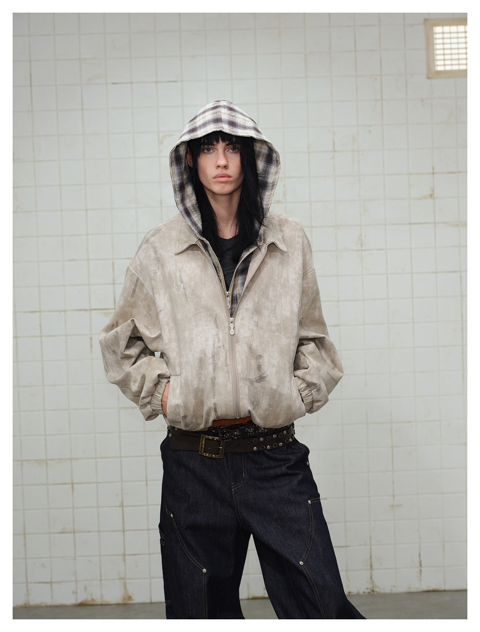 Model wearing khaki distressed zip jacket with plaid hood up, hands in pockets, with dark jeans and a studded belt