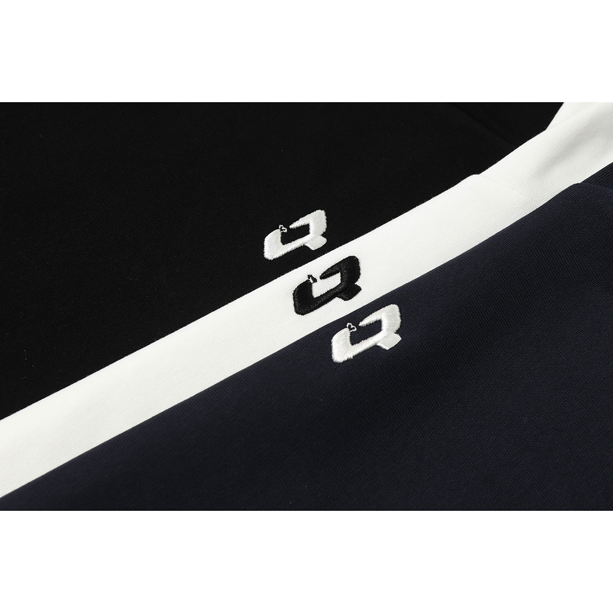 Close-up of black and navy fabric separated by a white diagonal stripe, each with a small embroidered emblem.